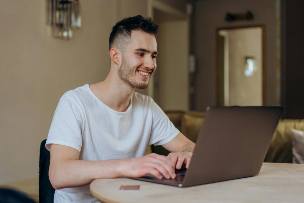 pexels photo 6969619 6969619 Young man smiling while online shopping with laptop indoors at home.